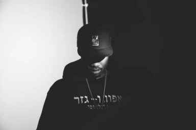 Monochrome portrait of a man wearing a black hoodie and a baseball cap with low-key studio lighting