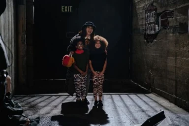 An adult woman and two children with voluminous curly hair pose together in front of a dark stage door exit in Los Angeles.