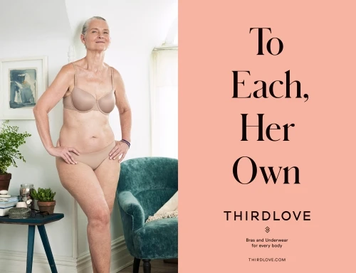 Mature woman in bra and underwear poses in a room next to a blue chair and pink advertising text for Third Love brand.