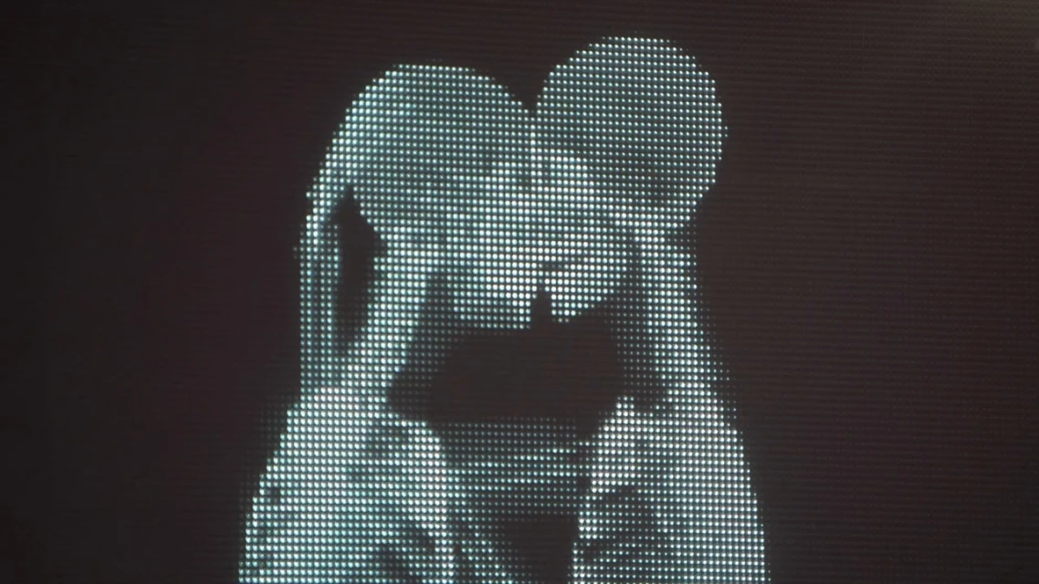 Pixelated image of two figures, likely adults, creating a heart shape with their heads on a dark background, possibly a digital art piece.