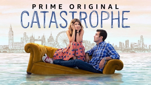 Man and woman are sitting on a yellow couch in the middle of water against a city skyline, promoting the show 'Catastrophe'.