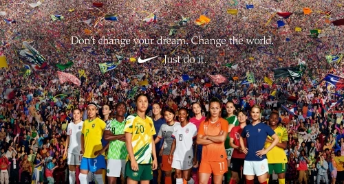 Group of female soccer players standing together on a field with crowd and flags, wearing sports uniforms, Nike logo, and 'Just do it.' text.