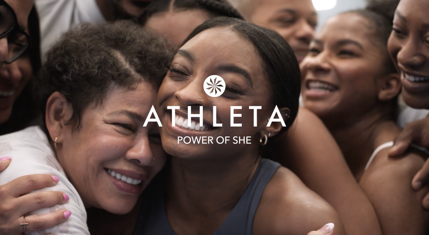 Group of smiling women embracing in a close-up shot with the Athleta logo and 'Power of She' text, promoting women's fitness and apparel.