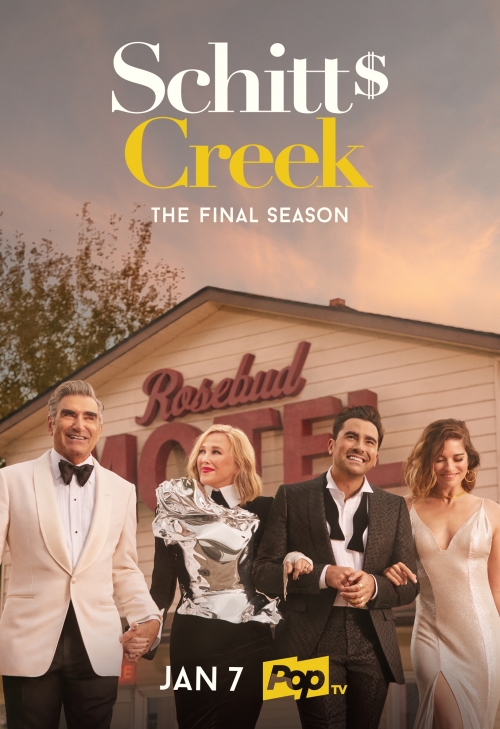 Promotional shot from Schitt's Creek showing four smiling adults in formal wear standing in front of the Rosebud Motel building.