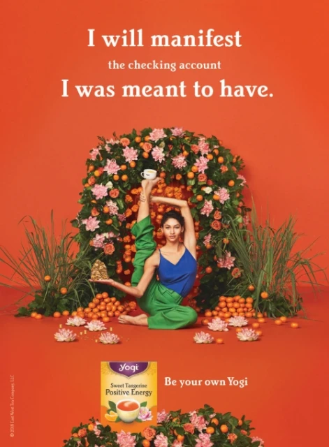 Adult female in yoga pose surrounded by flowers and tangerines, advertising Yogi Sweet Tangerine Positive Energy tea against orange backdrop.