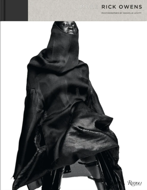 Fashion photography showcasing 'More Rick Owens' book cover, featuring a model in a dark, draped hooded garment against a white background.