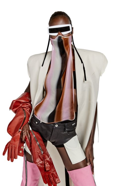 Fashion shot featuring a model in a white coat, sunglasses, and colorful top, accessorized with red gloves and pink boots against a white background.