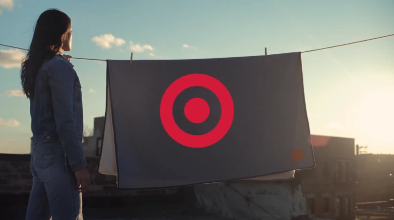 Woman in denim jacket standing on a rooftop beside a laundry line with a grey blanket featuring a red target logo.