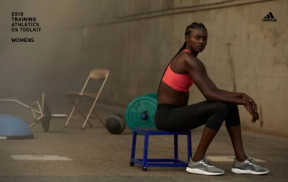 Black female athlete sitting on a blue gym box wearing a coral sports bra and dark leggings in an industrial setting