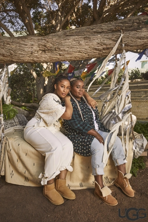 Two women sitting together on a decorated tree swing wearing casual clothing and tan boots