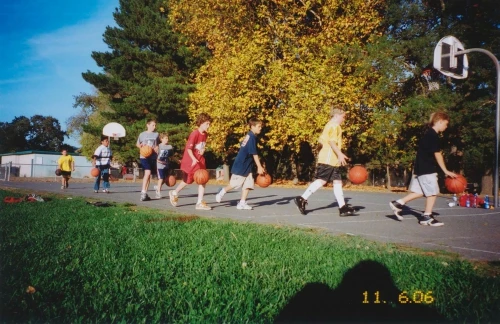 Group of children dribbling basketballs on an outdoor court with trees in the background on a sunny day. Youth sports.