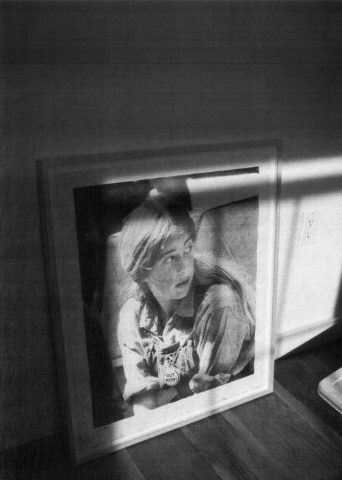 Black and white photograph of a framed portrait of a young person with short hair indoors, illuminated by sunlight from a window.