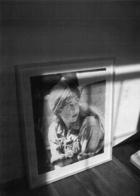 Black and white photograph of a framed portrait of a young person with short hair indoors, illuminated by sunlight from a window.