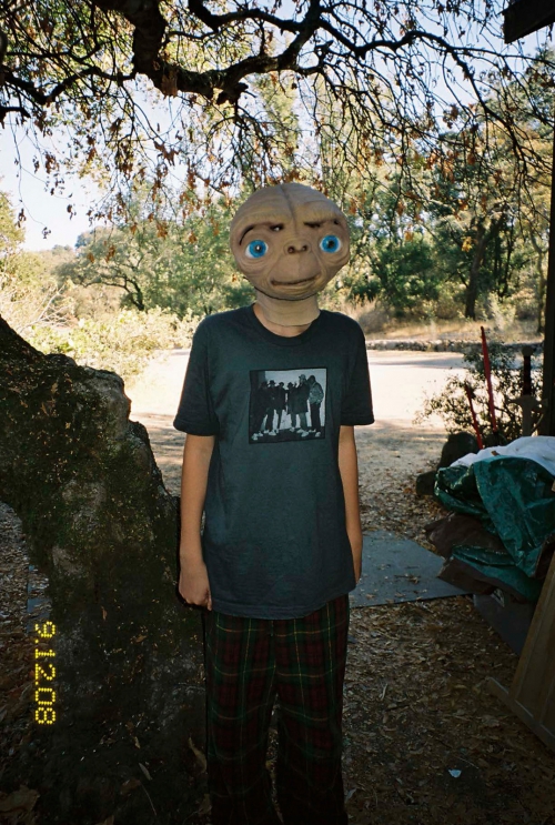 Person in E.T. mask with a t-shirt stands outside with trees and a date stamp of 9.12.08 on the film roll, capturing a nostalgic vibe.