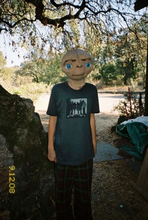 Person in E.T. mask with a t-shirt stands outside with trees and a date stamp of 9.12.08 on the film roll, capturing a nostalgic vibe.