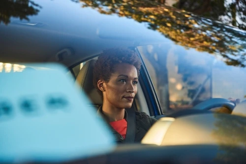 African-American woman driving car, safety belt, natural light, blurry background, short hair, professional, confident expression.