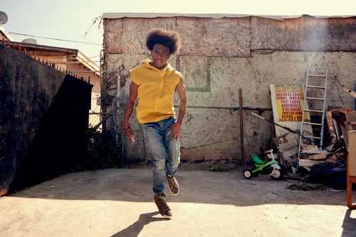 Young adult in casual wear walks toward the camera in an outdoor urban setting with a weathered wall backdrop, capturing a candid moment.