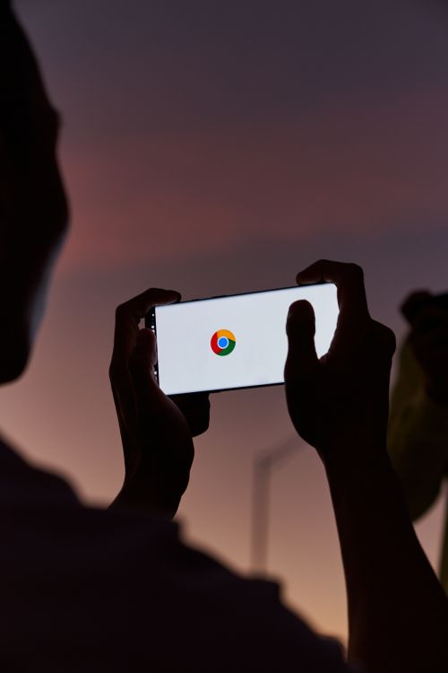 Silhouette of a person holding a phone displaying the Chrome logo against a dark twilight sky, showcasing technology and connectivity.