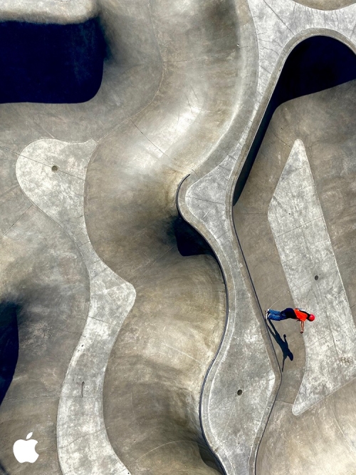 Aerial shot of a person in a red shirt skateboarding in a concrete skatepark on a sunny day, showcasing urban sport and recreation.