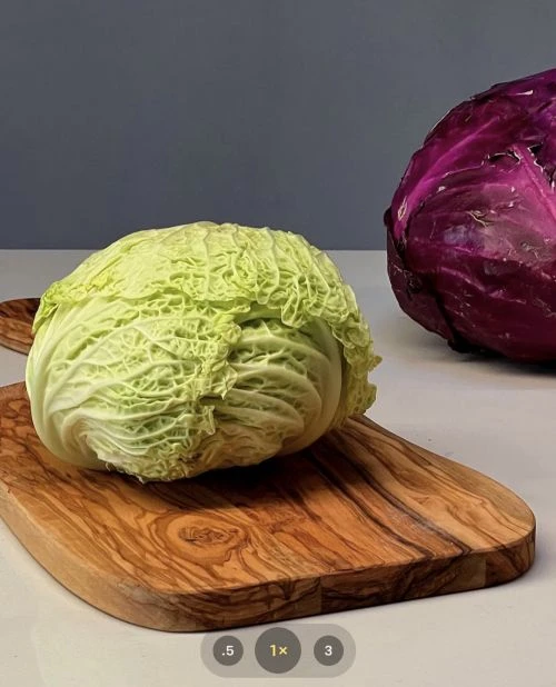 Savoy cabbage on a wooden cutting board with a red cabbage in the background on a white table against a gray background.