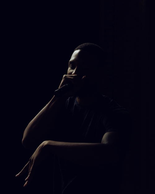 Dark portrait of a Black man singing with a microphone, wearing a t-shirt, dramatic lighting, dark background, artistic mood.