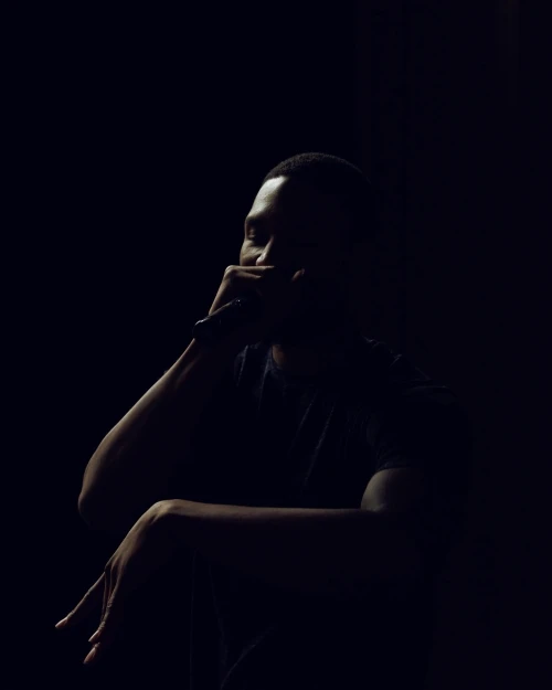 Dark portrait of a Black man singing with a microphone, wearing a t-shirt, dramatic lighting, dark background, artistic mood.