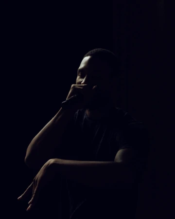 Dark portrait of a Black man singing with a microphone, wearing a t-shirt, dramatic lighting, dark background, artistic mood.