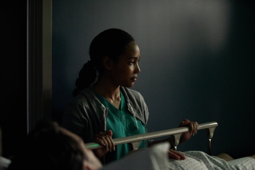 Healthcare scene featuring a female medical professional in scrubs at a hospital bedside, attending to a patient with care.