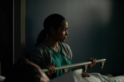 Healthcare scene featuring a female medical professional in scrubs at a hospital bedside, attending to a patient with care.