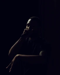 A dark, moody portrait of a Black man singing into a microphone in low-key lighting by photographer Jake Michaels.