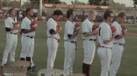 Baseball team players in white uniforms holding their caps against their chests on a field by Jake Michaels