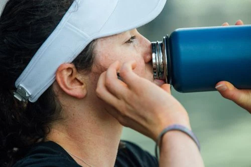 Close-up portrait of a woman wearing a white visor drinking from a blue water bottle outdoors.