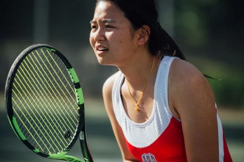 Young female tennis player holding a black and green racket on an outdoor court