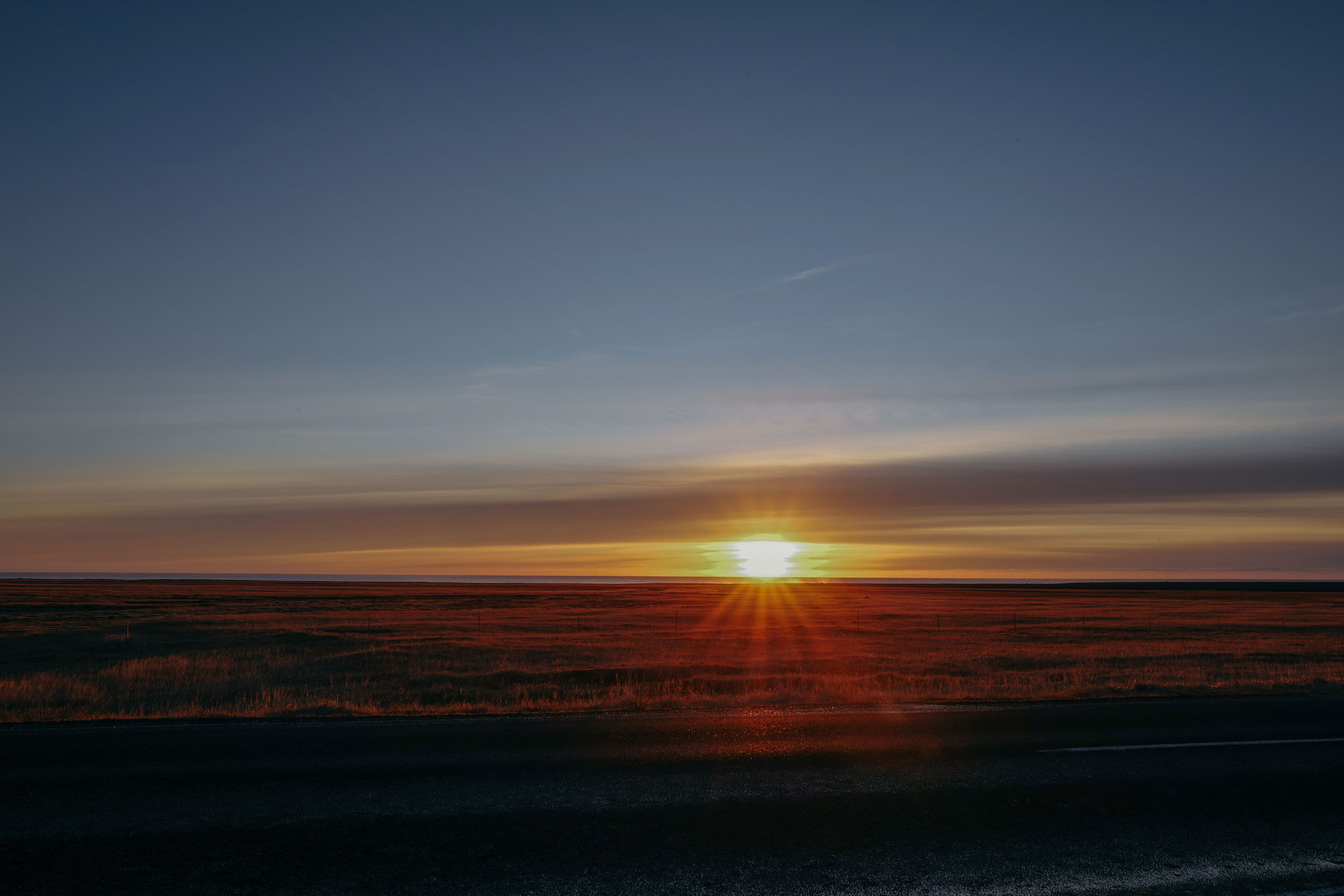 Horizon view of a setting sun creating a beautiful color gradient across the sky and illuminating a grassy field in the distance.