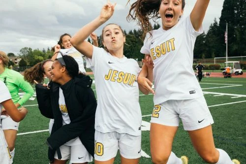 Group of young female soccer players in white sportswear celebrating and jumping on an outdoor sports field