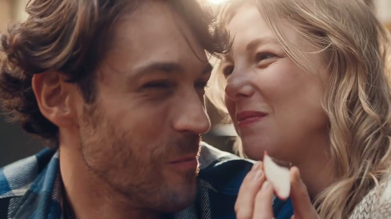 Close-up of a woman feeding an apple slice to a man. The couple are smiling and interacting, with a shallow depth of field.