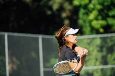 Female tennis player in black top and white visor swinging racket during outdoor match