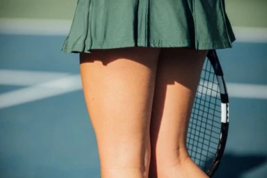 Close-up of a tennis player wearing a green pleated skirt and holding a tennis racket on a court.