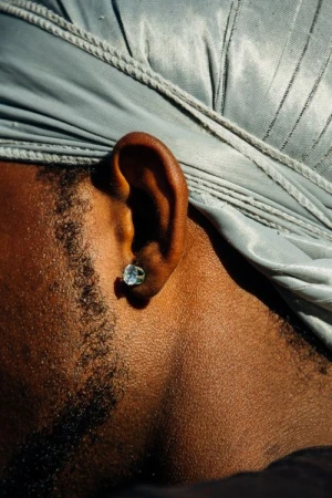 Close-up portrait of a Black man wearing a shiny silver durag and a sparkling diamond stud earring.