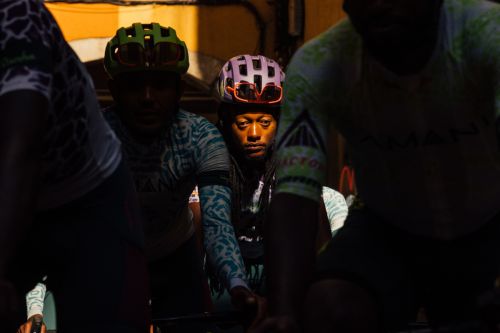 Cyclists wearing helmets and athletic gear are positioned in front of a dark building, creating a striking image focused on sports.