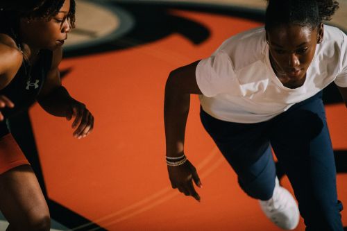 Two adult female athletes on a wrestling mat in action wearing athletic wear with focused expressions. Sports and fitness theme.