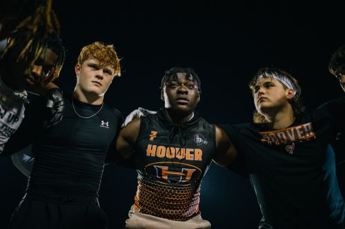 Group of high school football players standing together wearing team jerseys in a low angle shot against a dark background.