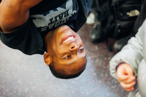 Smiling African-American man wearing a printed T-shirt, with other people visible in the background, in a candid indoor setting.