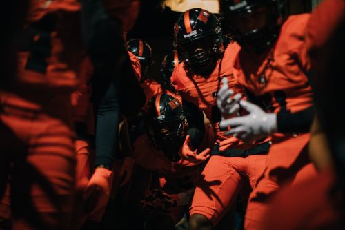 A group of football players in orange uniforms and helmets walking together, creating a sense of teamwork and determination.