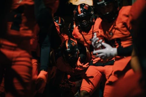 A group of football players in orange uniforms and helmets walking together, creating a sense of teamwork and determination.