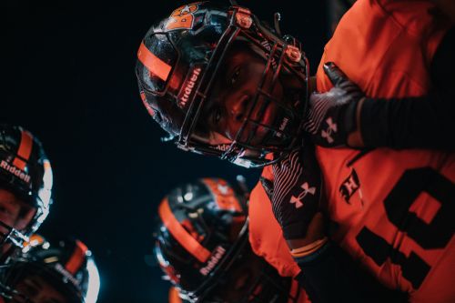 American football players wearing helmets and uniforms huddle close on a dark sports field, showcasing team spirit and camaraderie.