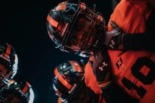 American football players wearing helmets and uniforms huddle close on a dark sports field, showcasing team spirit and camaraderie.