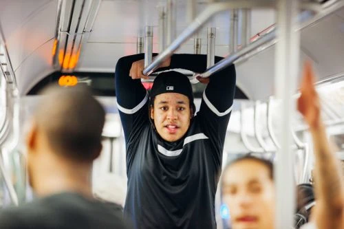 Man hanging on subway handrails in athletic wear, featuring a diverse group of passengers and urban transit setting.