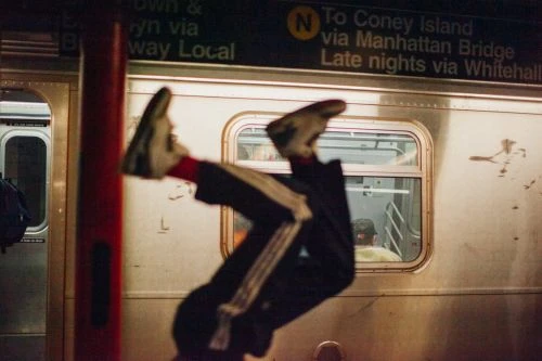 Person in mid-air performing a stunt at a subway station with a blurred train in the background. The image focuses on movement and urban energy.