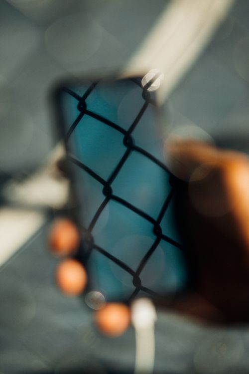 Close-up shot of a person holding a blurred smartphone with chain-link reflection, creating an abstract and textured visual effect.